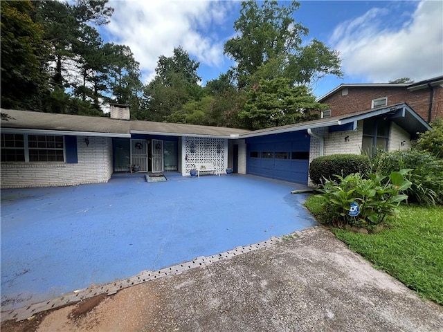 ranch-style home featuring an attached garage, brick siding, driveway, and a chimney