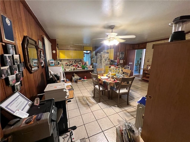 dining space with light tile patterned floors, wood walls, and ceiling fan