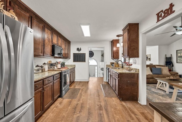 1464 Fieldstone Ct, Winder, GA 30680 - kitchen featuring appliances with stainless steel finishes, light wood-type flooring, ceiling fan, light stone counters, and dark brown cabinets