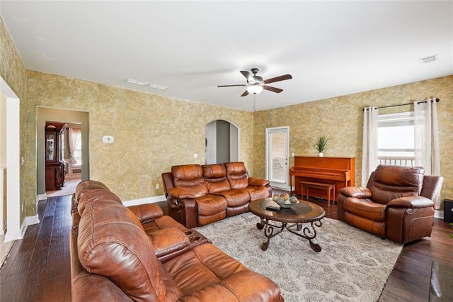 living room with arched walkways, dark wood finished floors, a ceiling fan, wallpapered walls, and baseboards