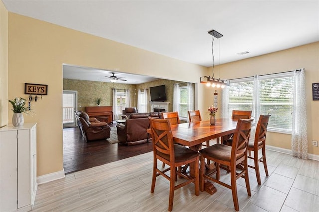 dining area with baseboards, a fireplace, light wood-type flooring, and ceiling fan