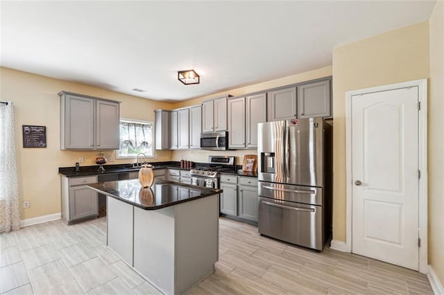 kitchen with stainless steel appliances, gray cabinets, dark countertops, baseboards, and a kitchen island