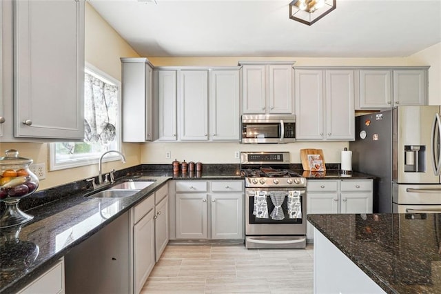 kitchen with appliances with stainless steel finishes, a sink, dark stone countertops, and gray cabinets