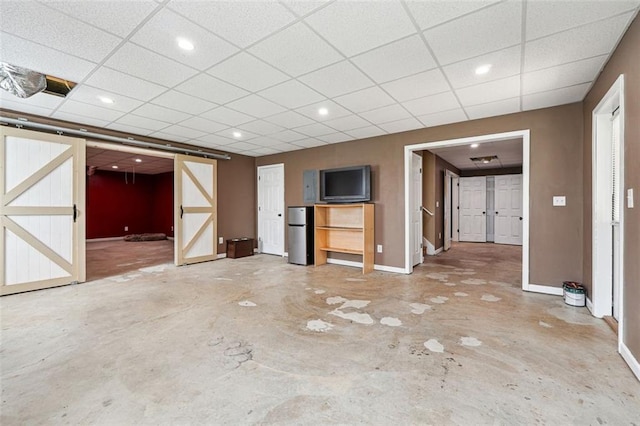 unfurnished living room featuring baseboards, unfinished concrete flooring, and a paneled ceiling