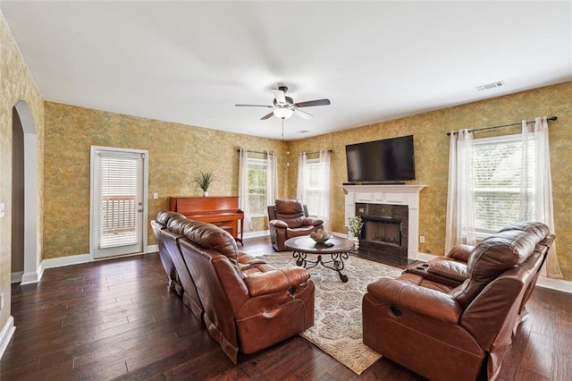 living area featuring arched walkways, a ceiling fan, a high end fireplace, dark wood-type flooring, and baseboards