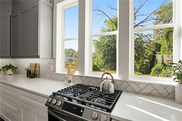 kitchen with range with gas stovetop, light stone countertops, gray cabinets, and backsplash