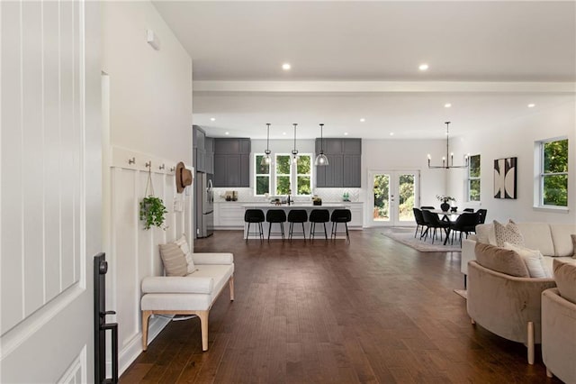 living room featuring an inviting chandelier, beamed ceiling, and dark wood-type flooring