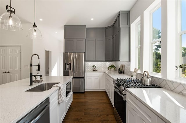 kitchen featuring sink, tasteful backsplash, light stone countertops, pendant lighting, and appliances with stainless steel finishes