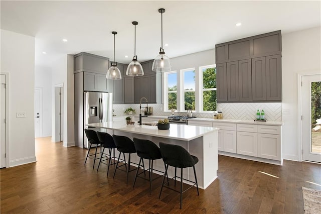 kitchen with a center island with sink, tasteful backsplash, a kitchen bar, gray cabinets, and appliances with stainless steel finishes