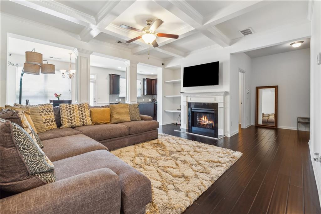 living room featuring coffered ceiling, beamed ceiling, dark wood-type flooring, and ceiling fan with notable chandelier