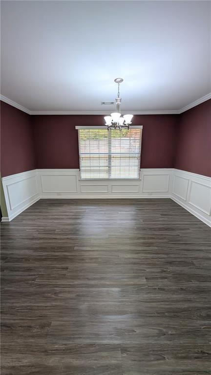 unfurnished dining area featuring dark wood-type flooring, ornamental molding, and a chandelier