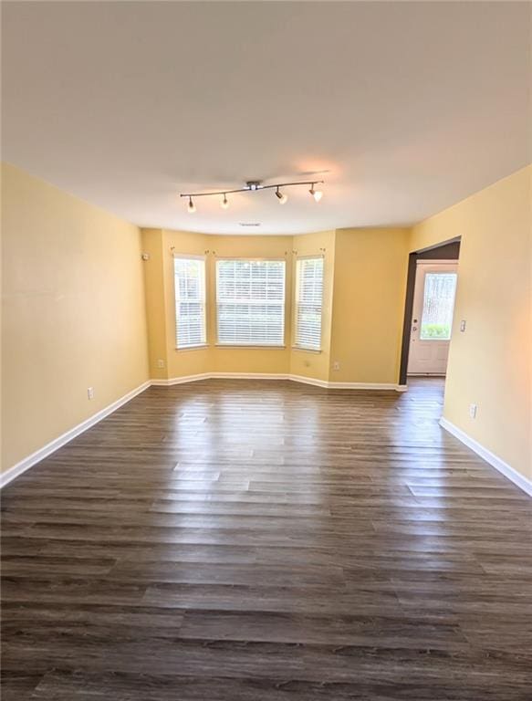 spare room featuring a healthy amount of sunlight, track lighting, and dark hardwood / wood-style flooring