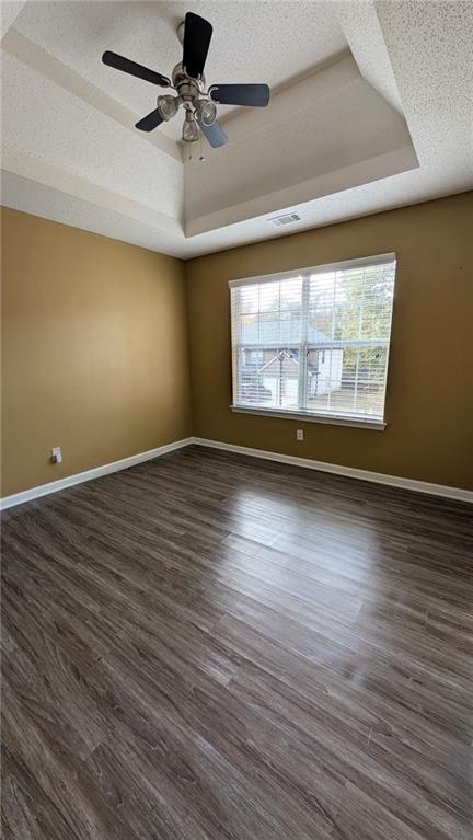 unfurnished room with dark wood-type flooring, ceiling fan, a raised ceiling, and a textured ceiling