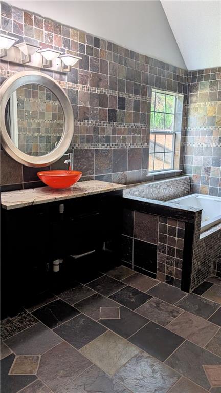 bathroom featuring vanity, tile walls, vaulted ceiling, and a relaxing tiled tub