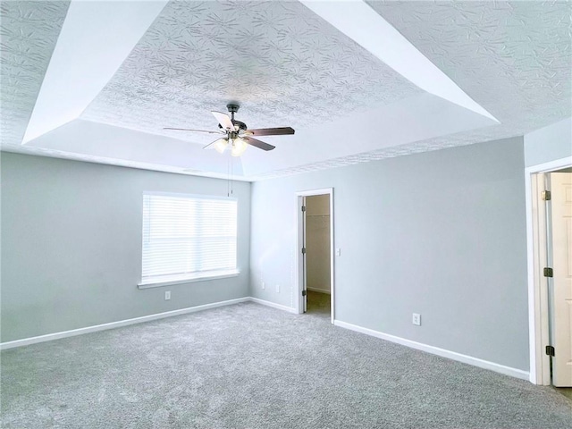 empty room with ceiling fan, carpet floors, a textured ceiling, and a tray ceiling