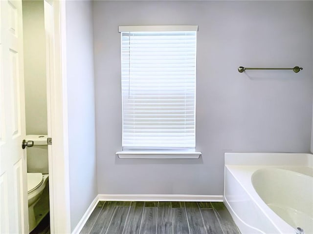 bathroom with a washtub, hardwood / wood-style floors, a wealth of natural light, and toilet