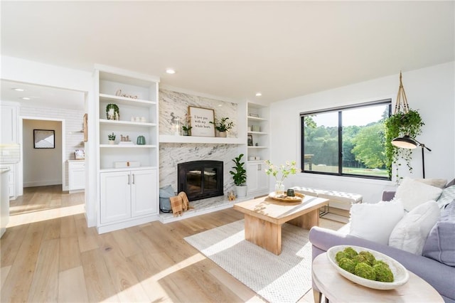 living area featuring recessed lighting, a premium fireplace, built in shelves, and light wood-style flooring