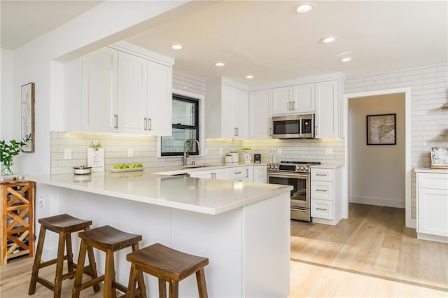 kitchen featuring a peninsula, light wood-style flooring, a sink, appliances with stainless steel finishes, and a kitchen breakfast bar