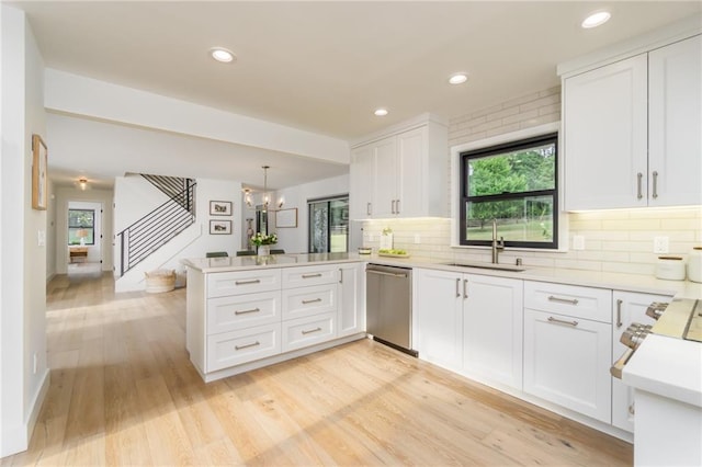 kitchen with a sink, stainless steel dishwasher, a peninsula, white cabinets, and light countertops