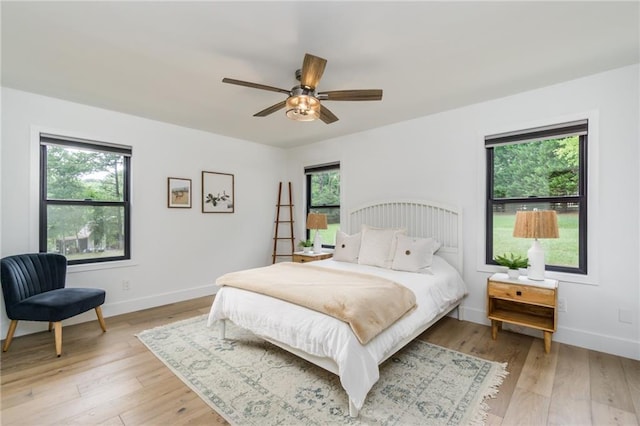 bedroom featuring multiple windows, baseboards, light wood-type flooring, and ceiling fan