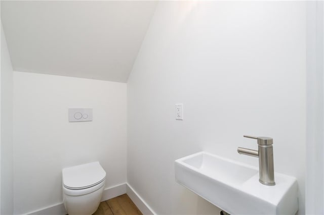 bathroom with toilet, lofted ceiling, a sink, wood finished floors, and baseboards