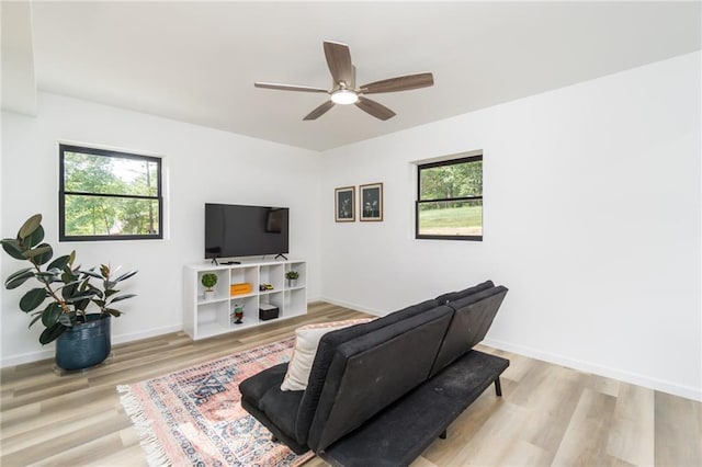 living area with a wealth of natural light, ceiling fan, baseboards, and light wood-style floors