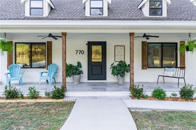 entrance to property featuring a porch, brick siding, and a shingled roof