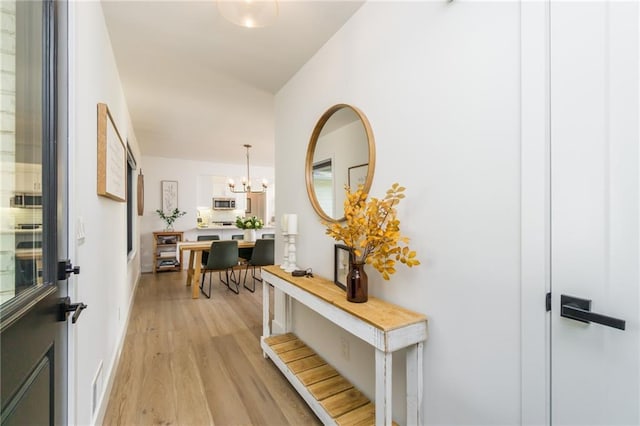 hall featuring a notable chandelier, light wood-style flooring, and baseboards