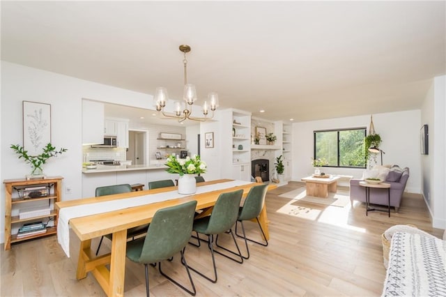 dining room with an inviting chandelier, baseboards, light wood finished floors, and a large fireplace