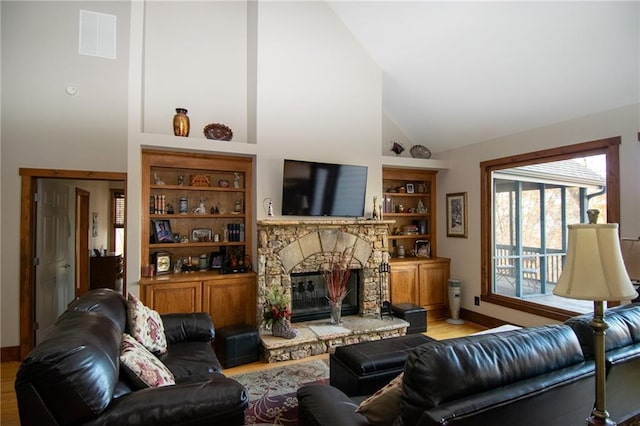 living room with high vaulted ceiling, a stone fireplace, built in features, and light wood-type flooring