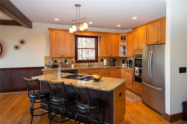 kitchen with light stone countertops, appliances with stainless steel finishes, a kitchen island with sink, and a kitchen bar