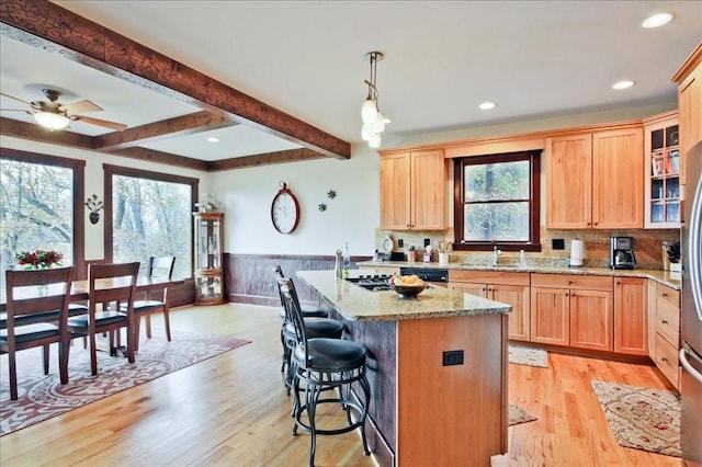 kitchen with a kitchen bar, light stone counters, a center island with sink, beam ceiling, and light hardwood / wood-style flooring