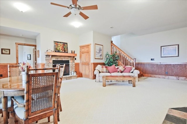 carpeted living room with ceiling fan, a fireplace, and wood walls