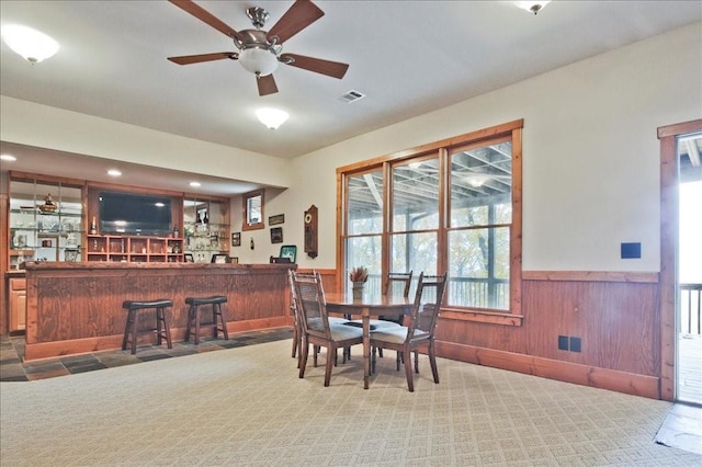 dining space featuring indoor bar, carpet flooring, and ceiling fan