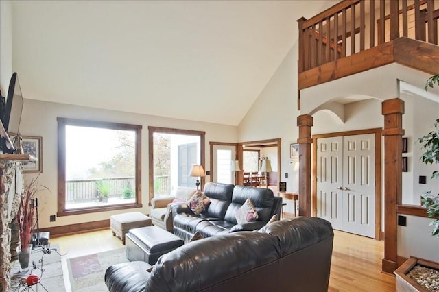 living room with ornate columns, a wealth of natural light, high vaulted ceiling, and light hardwood / wood-style flooring