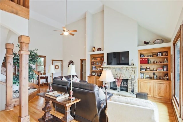 living room featuring built in shelves, high vaulted ceiling, a fireplace, and light hardwood / wood-style floors