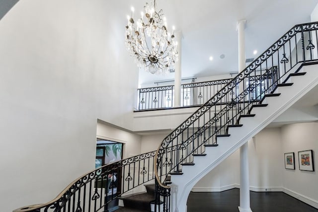 staircase featuring an inviting chandelier, wood finished floors, a towering ceiling, and baseboards