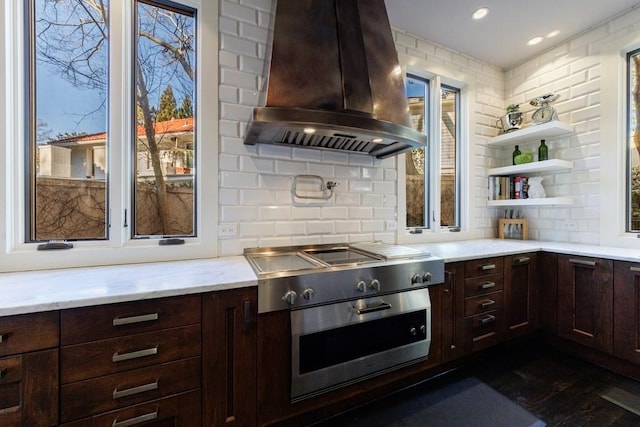 kitchen featuring dark brown cabinets, backsplash, island exhaust hood, and light stone countertops