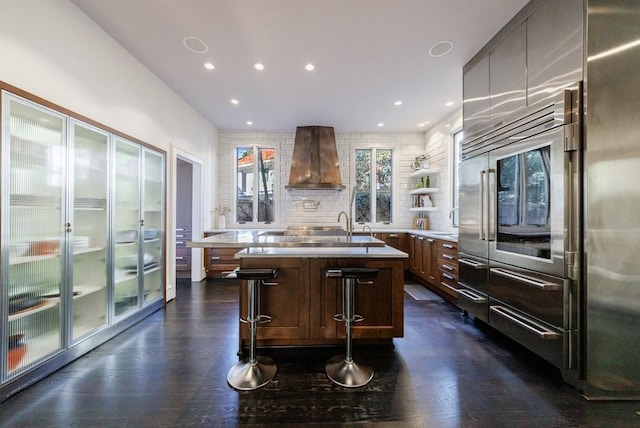 kitchen with light countertops, wall chimney range hood, dark wood finished floors, and decorative backsplash