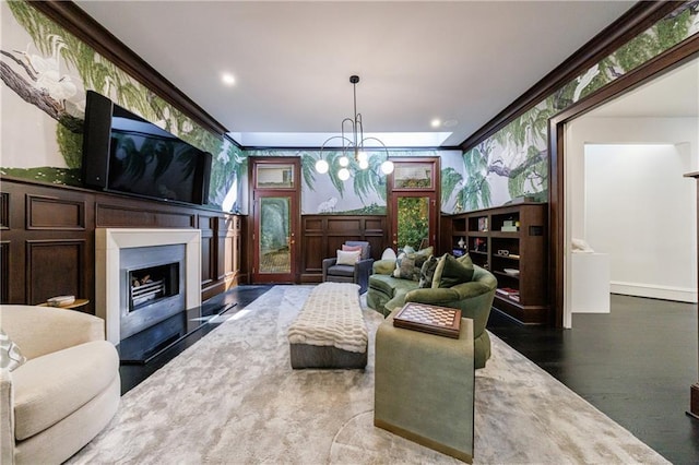 living room featuring wallpapered walls, a fireplace with raised hearth, wood finished floors, an inviting chandelier, and crown molding