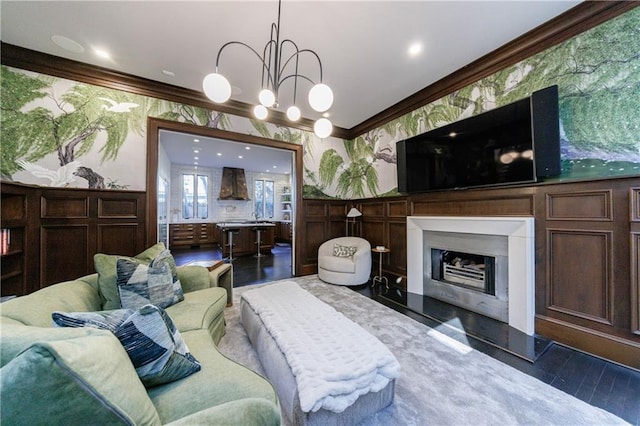 living area featuring a fireplace, wood finished floors, ornamental molding, wallpapered walls, and an inviting chandelier