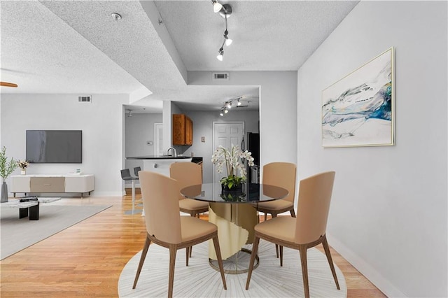 dining space with rail lighting, sink, a textured ceiling, and light wood-type flooring