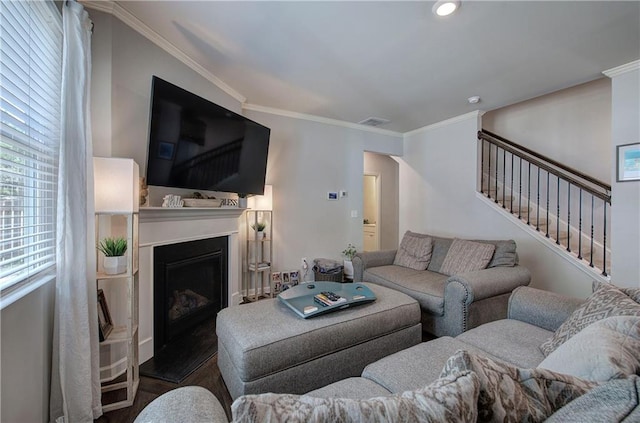 living room featuring a fireplace with raised hearth, wood finished floors, visible vents, stairs, and crown molding