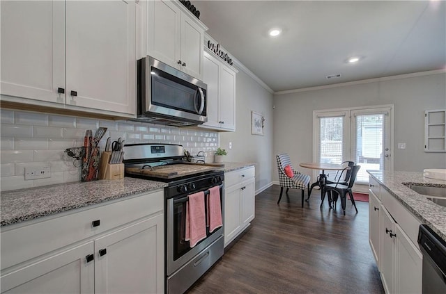 kitchen with dark wood-type flooring, white cabinets, ornamental molding, appliances with stainless steel finishes, and decorative backsplash