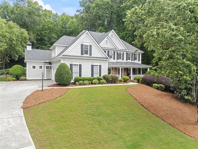 view of front of property with concrete driveway, a porch, a standing seam roof, a front yard, and roof with shingles