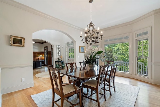 dining space with arched walkways, a chandelier, crown molding, light wood-style flooring, and baseboards