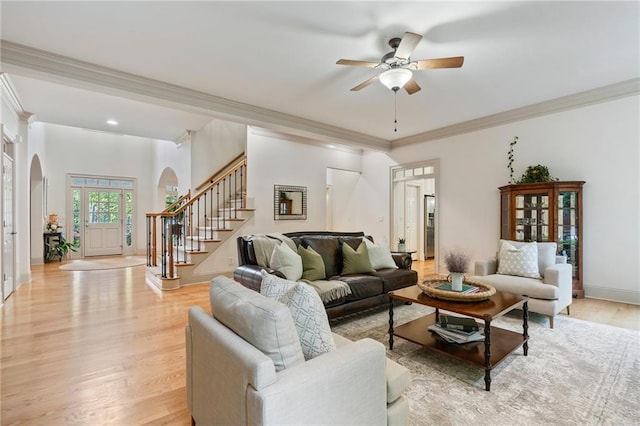 living area with arched walkways, crown molding, light wood-style flooring, stairs, and a ceiling fan