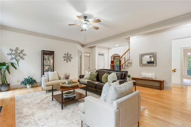 living room featuring ceiling fan, stairs, ornamental molding, light wood finished floors, and baseboards