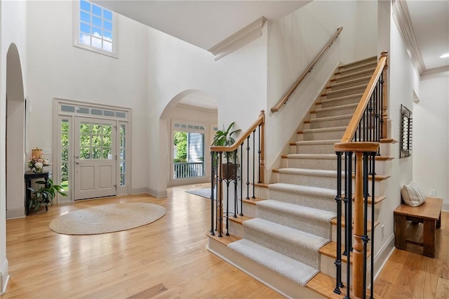 foyer with arched walkways, wood finished floors, a high ceiling, stairway, and baseboards