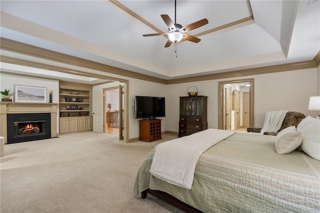 bedroom with a raised ceiling, a fireplace with flush hearth, light colored carpet, and ensuite bath